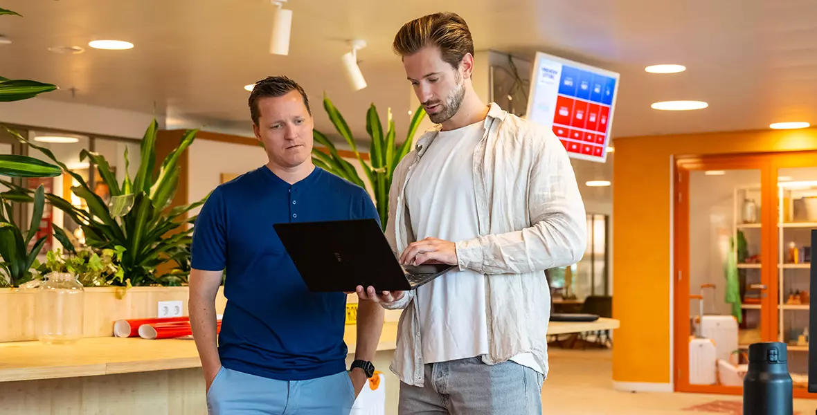 Twee collega’s staan op kantoor. De ene collega kijkt mee op de laptop van de andere collega.