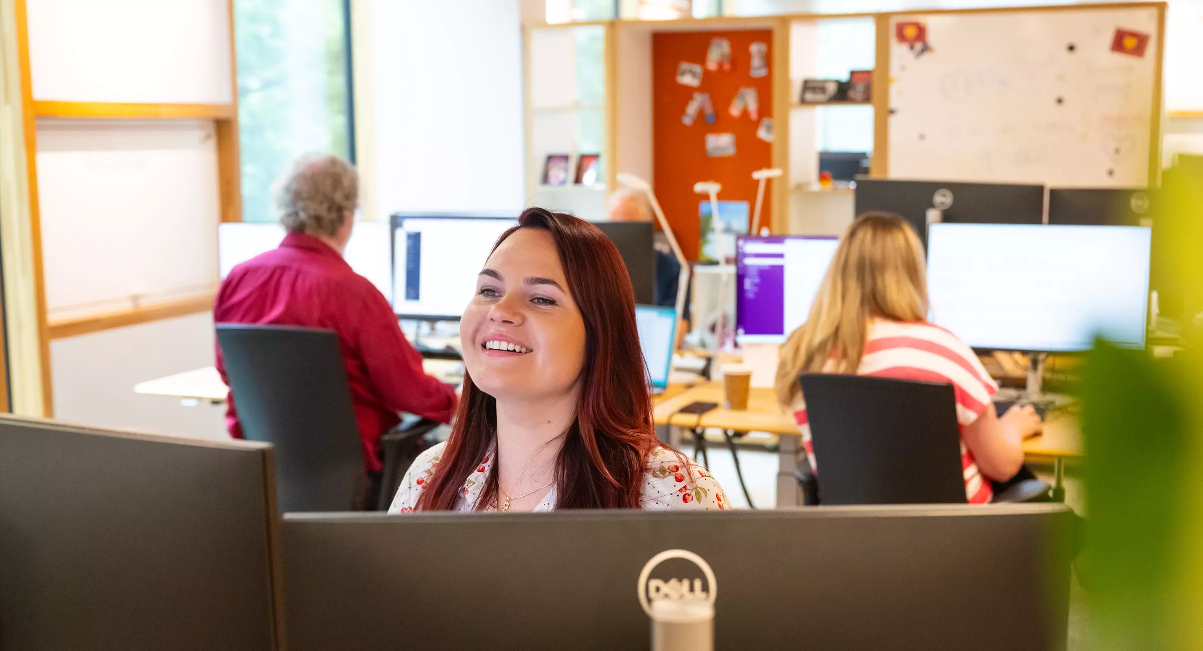 Medewerker van de Postcode Loterij achter de computer. Op de achtergrond zijn collega's aan het werk.