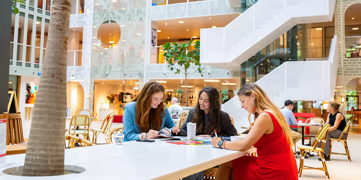 Drie collega's van de Postcode Loterij lachend rond een tafel aan het werk.