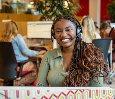 Lachende vrouw zit met headset op te werken bij Ledenservice.