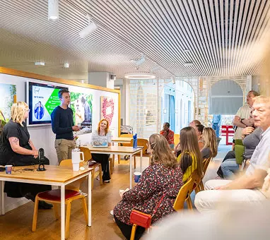 Een collega geeft een presentatie aan andere collega's in de kantine van het kantoor van de Postcode Loterij.