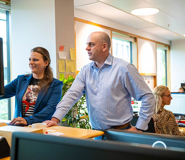 Twee collega's staan pratend aan een bureau naar een monitor te kijken.